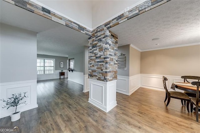 dining room featuring decorative columns, wood finished floors, a wainscoted wall, and a textured ceiling