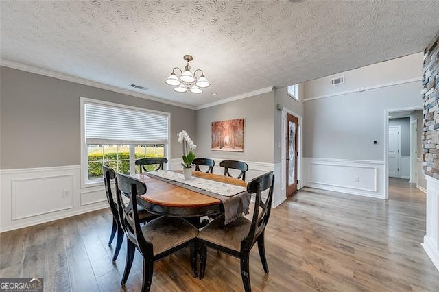 dining space with visible vents, wood finished floors, a textured ceiling, and a chandelier