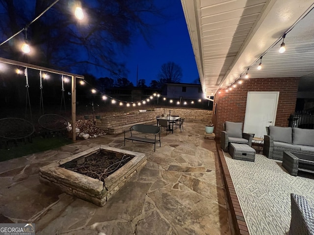 patio at night featuring an outdoor living space with a fire pit and fence