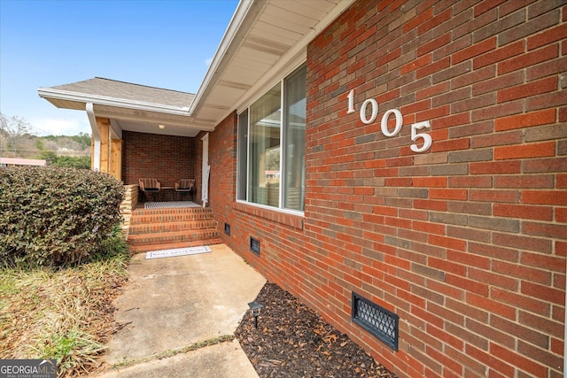 property entrance with brick siding, a porch, and roof with shingles