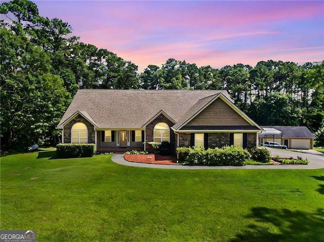 single story home with an outbuilding, driveway, a shingled roof, stone siding, and a lawn