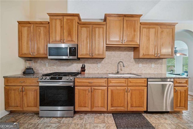 kitchen with a sink, light stone counters, tasteful backsplash, stainless steel appliances, and brown cabinetry