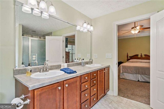 ensuite bathroom featuring a sink, connected bathroom, a textured ceiling, and a stall shower