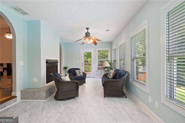 living area featuring visible vents, a fireplace, arched walkways, ceiling fan, and a textured ceiling