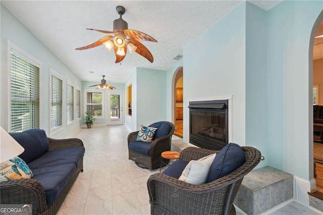 living area with arched walkways, a textured ceiling, a fireplace, and a ceiling fan