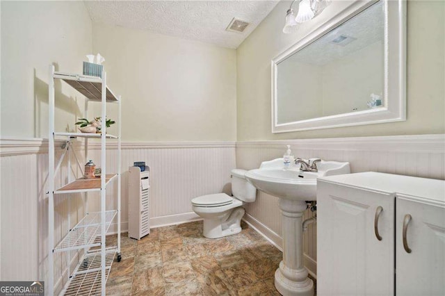 bathroom featuring visible vents, a textured ceiling, toilet, and a wainscoted wall