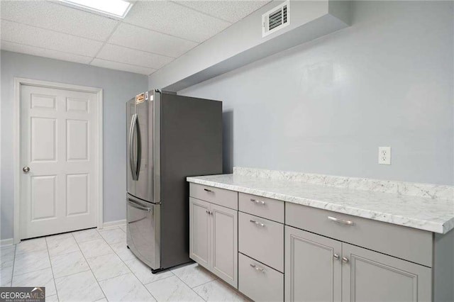 kitchen featuring visible vents, a drop ceiling, freestanding refrigerator, gray cabinetry, and marble finish floor