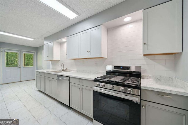 kitchen featuring tasteful backsplash, a drop ceiling, gray cabinets, stainless steel appliances, and a sink