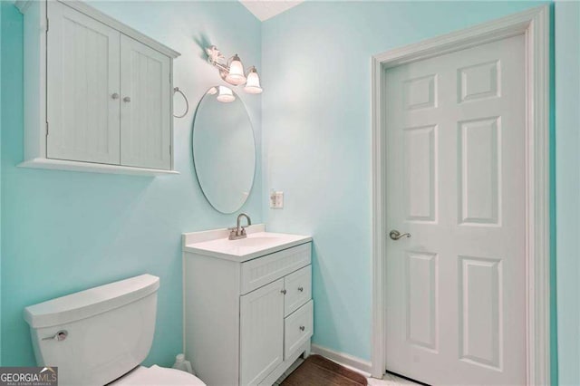 half bathroom featuring vanity, toilet, wood finished floors, and baseboards