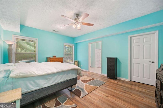 bedroom featuring ceiling fan, baseboards, a textured ceiling, and wood finished floors