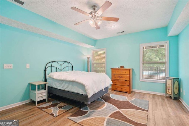 bedroom with a textured ceiling, wood finished floors, visible vents, and baseboards