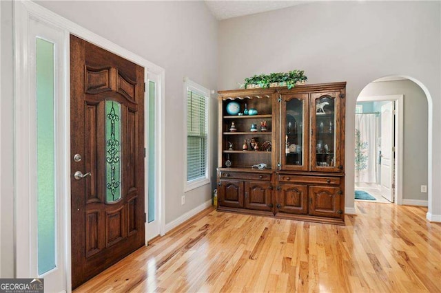 entrance foyer with baseboards, arched walkways, light wood-style floors, and a healthy amount of sunlight