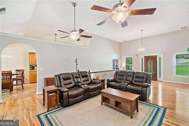 living room featuring light wood finished floors, ceiling fan, a wealth of natural light, arched walkways, and a textured ceiling