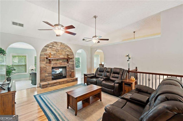 living area with visible vents, light wood-style flooring, a ceiling fan, a stone fireplace, and lofted ceiling