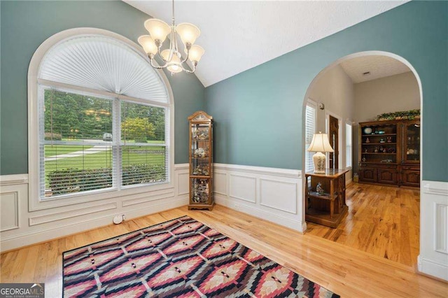 interior space with lofted ceiling, wainscoting, wood finished floors, arched walkways, and a notable chandelier