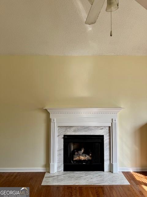 interior details featuring a fireplace, a textured ceiling, baseboards, and wood finished floors