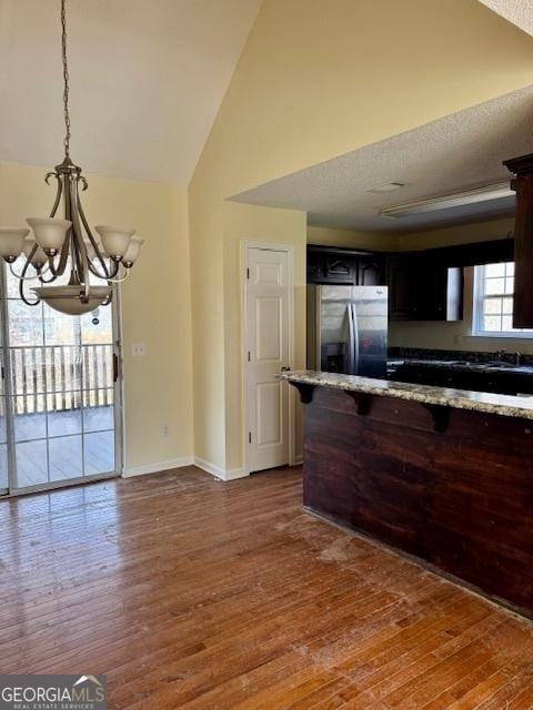 kitchen with baseboards, a chandelier, light stone counters, stainless steel refrigerator with ice dispenser, and wood finished floors