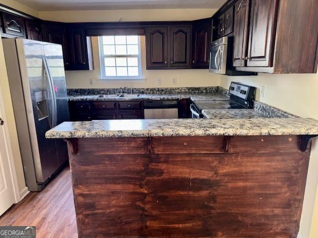 kitchen featuring light stone counters, a sink, light wood-style floors, appliances with stainless steel finishes, and a peninsula