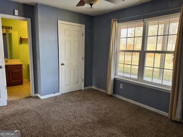 unfurnished bedroom with multiple windows, ensuite bath, baseboards, and carpet floors