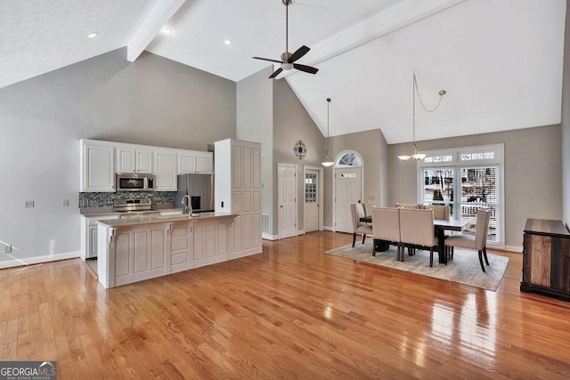 kitchen with beamed ceiling, decorative backsplash, light wood-style flooring, white cabinets, and stainless steel appliances