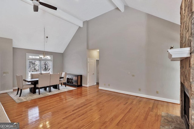 dining room with beam ceiling, a fireplace, light wood-type flooring, and baseboards