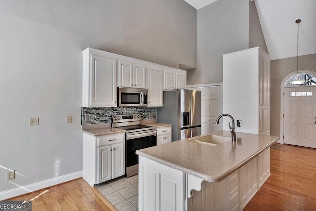 kitchen featuring a sink, backsplash, appliances with stainless steel finishes, white cabinets, and light wood finished floors