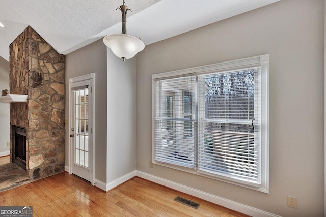 unfurnished dining area featuring wood finished floors, visible vents, baseboards, a fireplace, and a textured ceiling