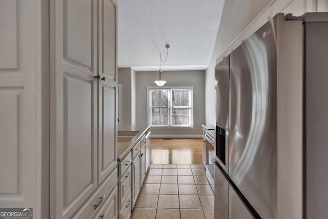 kitchen featuring baseboards, hanging light fixtures, stainless steel appliances, light tile patterned flooring, and a textured ceiling