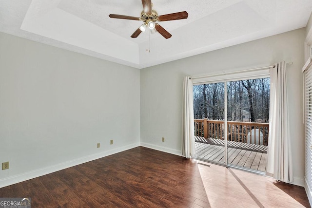 unfurnished room with baseboards, a ceiling fan, a tray ceiling, and wood finished floors