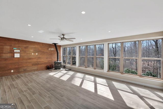 unfurnished living room featuring a wood stove, wooden walls, wood finished floors, and plenty of natural light