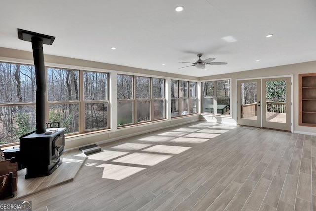 unfurnished sunroom featuring french doors, a wood stove, and ceiling fan