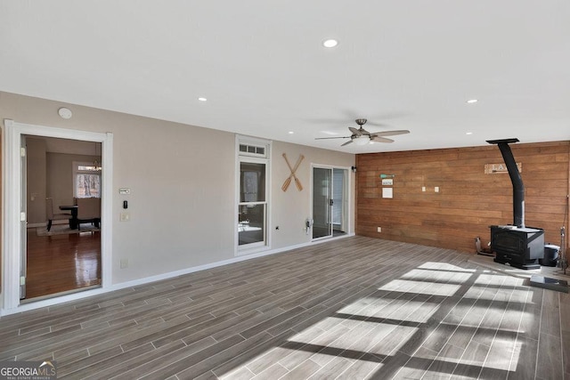 unfurnished living room featuring wooden walls, wood tiled floor, a wood stove, recessed lighting, and ceiling fan