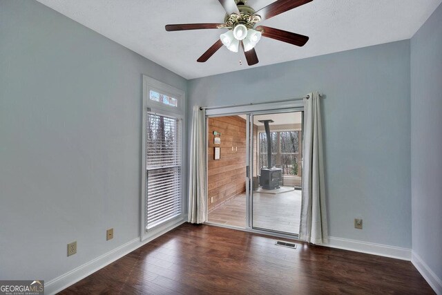 spare room featuring wood finished floors, visible vents, baseboards, a wood stove, and ceiling fan