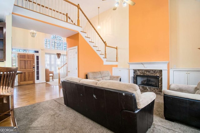 living room featuring wood finished floors, a high end fireplace, a towering ceiling, stairway, and ceiling fan