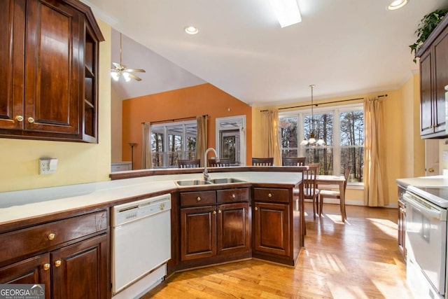 kitchen with white appliances, light wood finished floors, a peninsula, a sink, and vaulted ceiling