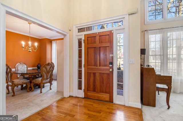 foyer entrance featuring wood finished floors, baseboards, a towering ceiling, crown molding, and a chandelier