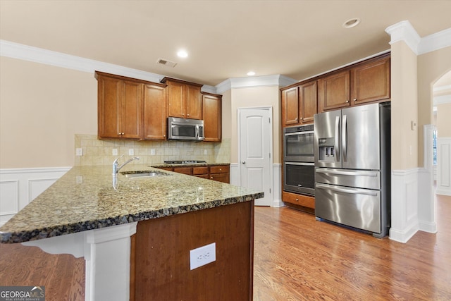 kitchen featuring a sink, dark stone countertops, stainless steel appliances, light wood-style floors, and a peninsula