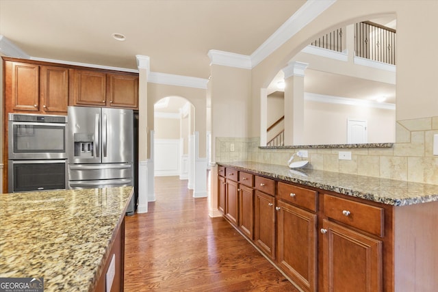 kitchen with light stone counters, stainless steel appliances, arched walkways, decorative backsplash, and dark wood-style flooring