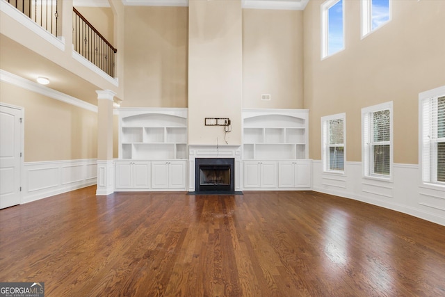 unfurnished living room featuring built in shelves, a wainscoted wall, visible vents, a premium fireplace, and dark wood-style flooring