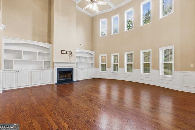 unfurnished living room featuring crown molding, a wainscoted wall, a fireplace, a ceiling fan, and dark wood-style flooring