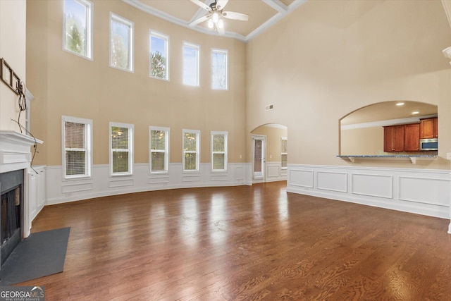 unfurnished living room featuring arched walkways, a fireplace with flush hearth, a healthy amount of sunlight, and a ceiling fan