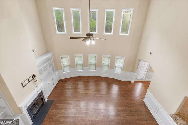 unfurnished living room with wood finished floors, a fireplace with flush hearth, ceiling fan, and a decorative wall