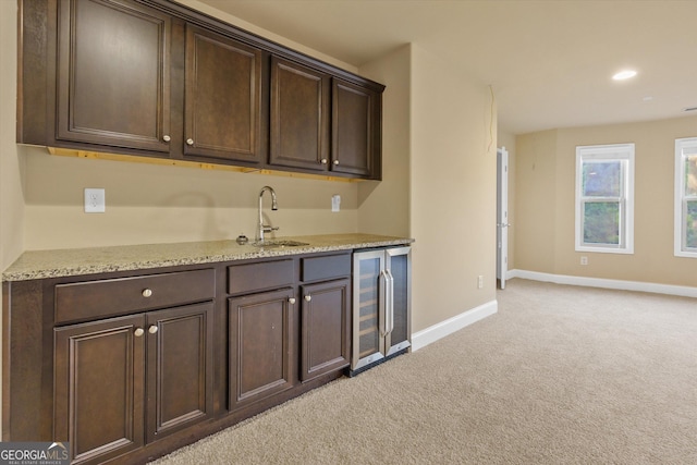 kitchen featuring dark brown cabinets, baseboards, wine cooler, light carpet, and a sink