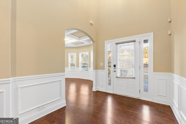 entryway featuring beamed ceiling, coffered ceiling, wood finished floors, arched walkways, and wainscoting