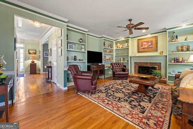 living room featuring wood finished floors, baseboards, ceiling fan, crown molding, and a brick fireplace