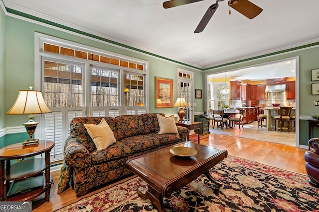 living room with ceiling fan, baseboards, ornamental molding, and light wood finished floors