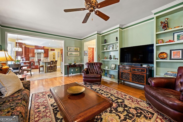 living room featuring built in features, ornamental molding, a ceiling fan, and light wood finished floors