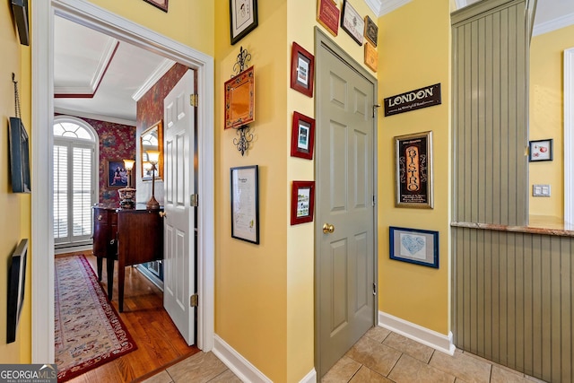 hall featuring light tile patterned floors, baseboards, and crown molding