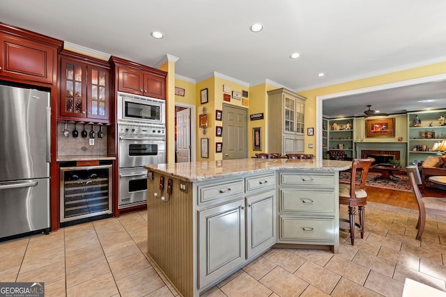 kitchen with beverage cooler, a kitchen island, stainless steel appliances, a fireplace, and crown molding