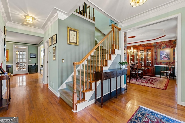 stairway featuring a notable chandelier, crown molding, baseboards, and wood finished floors